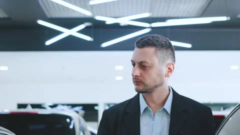 A man in formal attire examines different cars in a well-lit showroom, comparing Stock Footage 304712942