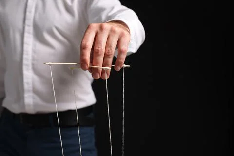 Man in formal outfit pulling strings of puppet on black background, closeup.. Stock Photos
