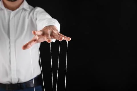 Man in formal outfit pulling strings of puppet on black background, closeup.. Stock Photos