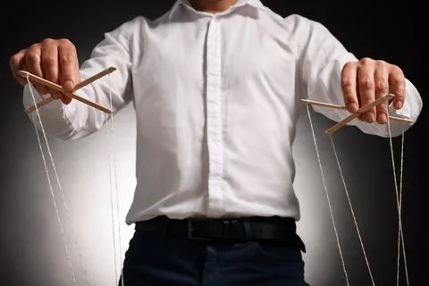 Man in formal outfit pulling strings of puppet on dark background, closeup Stock Photos