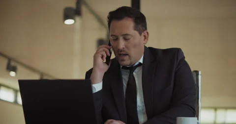 A man in a formal suit looking at a laptop screen while talking on the phone. Stock Footage 140205574