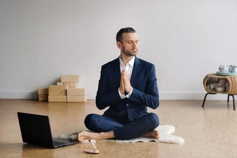 A man in a formal suit meditates while sitting in a fitness room with a laptop Stock Photos