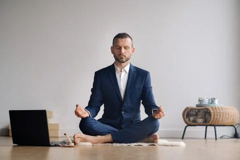 A man in a formal suit meditates while sitting in a fitness room with a laptop Stock Photos