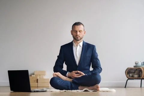 A man in a formal suit meditates while sitting in a fitness room with a laptop Stock Photos