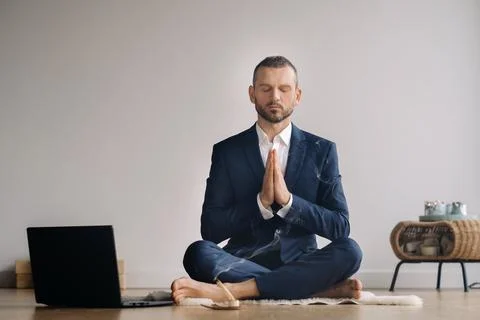 A man in a formal suit meditates while sitting in a fitness room with a laptop Stock Photos