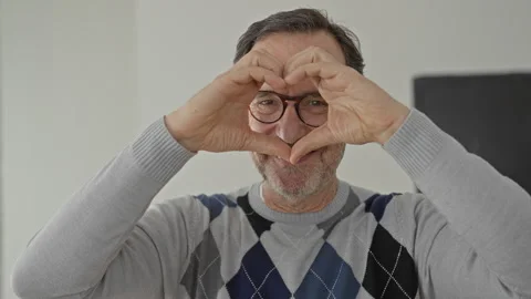 Man forms heart with hands through round glasses in building interior, smil.. Stock Footage 347874375