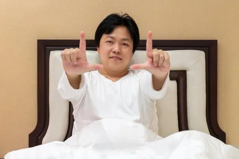 Man frames the scene with his hands while sitting on the bed, exploring how.. Stock Photos