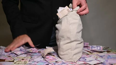 Man frantically stuffs large sack of Ukrainian cash, stark representation of Stock Footage 330488238