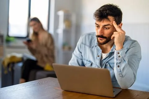 A man freelancer concentrates on digital tasks at home, facing mental overl.. 스톡 사진