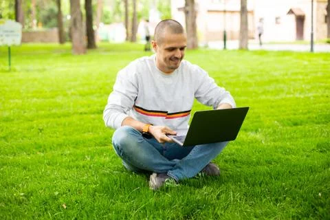 Man freelancer developer working on laptop sitting on lawn Stock Photos