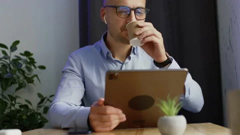 Man freelancer drinks cup of coffee working on tablet Stockbeeldmateriaal 205068799