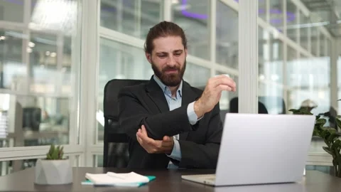 Man freelancer typing on laptop keyboard while feeling pain in elbow in office Stock Footage 257526159