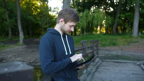 Man freelancer working on the lake with a tablet computer, image at sunset. The  Stock Footage 76739374
