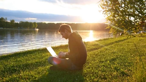 Man freelancer working on the lake with a tablet computer, image at sunset. The  Stock Footage 76740076