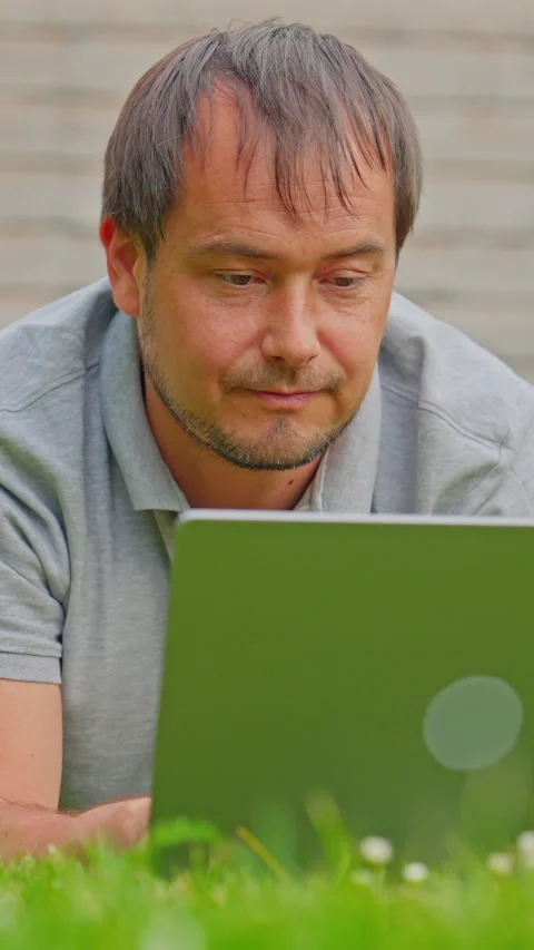 Man freelancer working on laptop outdoors lying down in park. Remote work Stock Footage 315972408