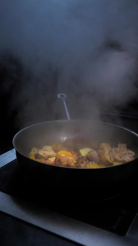 A man fries meat with vegetables adding broth to the pan making a lot of smoke. Stock Footage 309463186