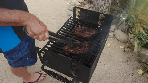A man fries two steaks on a small outdoor BBQ Stock Footage 133142850