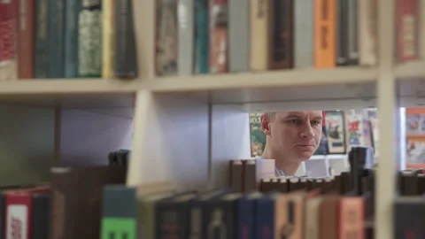A man in front of a bookcase in a library chooses a book Vídeo Stock 119961652