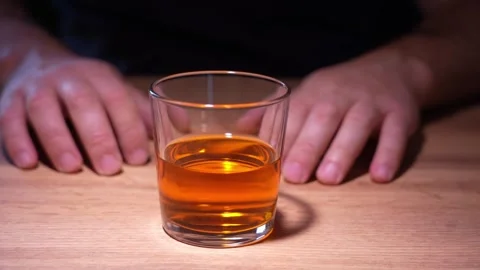 A man in front of a glass of alcohol struggles with the desire to drink an Stock Footage 342396868