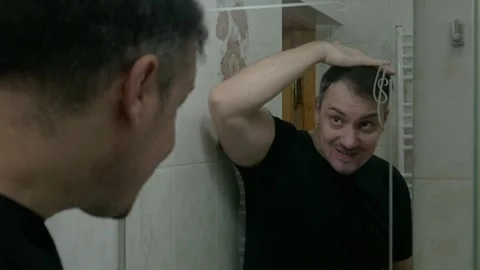 Man in front of the mirror gets angry when he fails to brush his hair Stock Footage 268224482