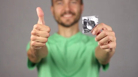 Man in front of raises on outstretched hand condom, hand makes gesture thumb up Video stock 94926833