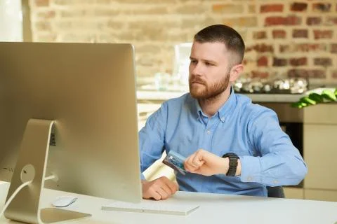 A man frowns looking at the display of the computer and holds a credit card. Stock Photos