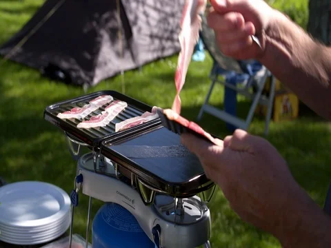 Man frying bacon on a camping on a portable gas stove, sunny day Stock Footage 76261453