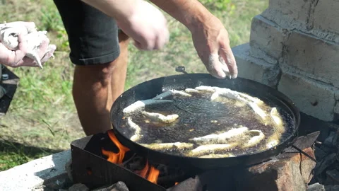 Man frying fish on open fire in cast iron pan outdoors Stock Footage 312522235