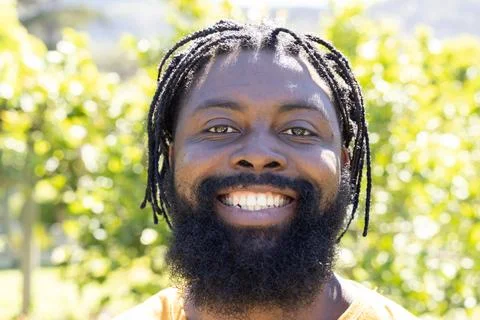Man with full beard and dreadlocks smiling and looking at camera in park wearing Stock Photos