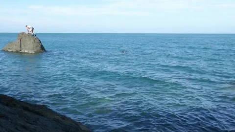A man funny climbs on a stone in the water and keeps his balance Stock Footage 293273634