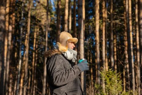 Man in fur hat and warm jacket drinking hot beverage in pine forest. Travel Fotos Stock