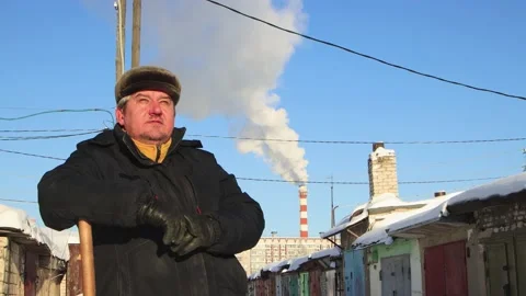 A man in a fur hat rests leaning on a wooden snow shovel. Stock Footage 224680222