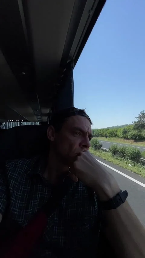 Man gazing out bus window during reflective rural journey with hand at chin Видео 344585411