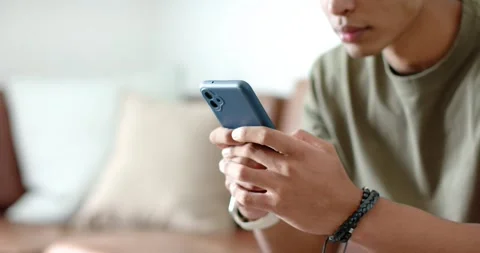Man is gazing at screen then is scrolling blue-cased smartphone on couch and is 動画素材 339652060