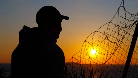 Man gazing at sunset behind barbed wire fence Stock Footage 302633401