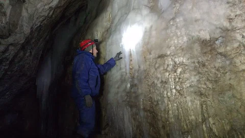 Man in gear and with a flashlight examines the ice on the wall of the cave Stock Footage 129495002