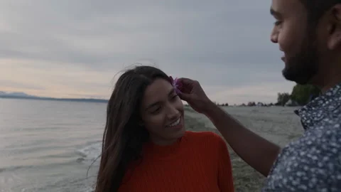 Man gently places a flower behind woman's ear on the beach at sunset Stock Footage 312708716