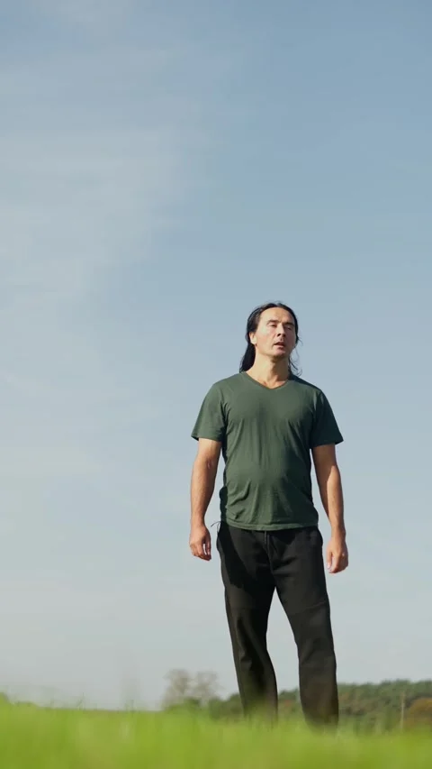 A Man Gently Strolling Through a Beautiful, Lush Green Field Beneath a Clear Stock Footage 308927785