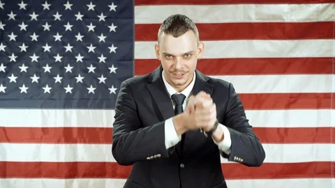 Man gesticulating and speaking against the background of the American flag Stock Footage 119569324