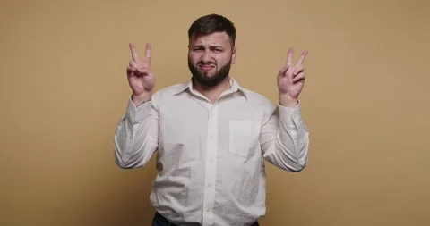 Man gestures with hands while making a face in front of a plain background Stockbeeldmateriaal 326797271