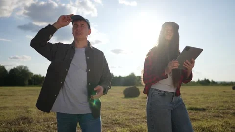 Man gestures while woman holds tablet in sunset field. Two farmers discuss data Stock Footage 342605315