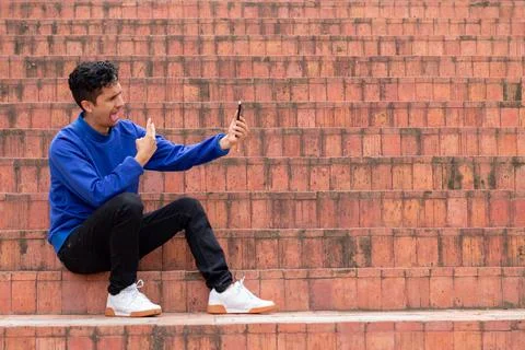 Man gesturing and taking a selfie. Sitting on orange stairs with space to write Stock Photos