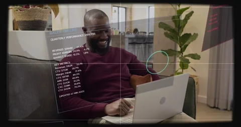 Man gesturing and tapping laptop on sofa, HUD panels appearing while reviewing Stock Footage 334031251