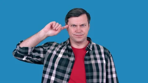 A man gesturing with a finger to his temple, wearing a plaid shirt. Stock Footage 148374999