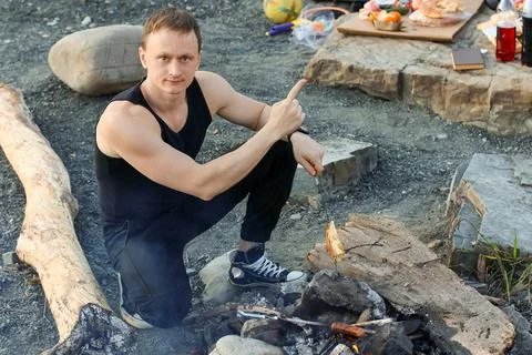 Man gesturing one while presenting grilled poultry over open flames. Stock Photos