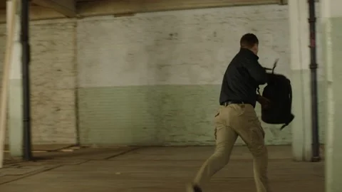 Man gets chased in a warehouse through an industrial door, in moody lighting. Me Stock Footage 199455609