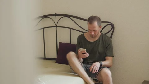 A man gets out of bed with a phone in his hand Vidéo 312063455