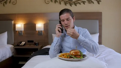 Man gets off phone and eats hamburger in hotel room 스톡 동영상 94266846