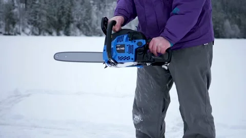 As a man gets ready to cut a hole in the ice, he starts the chainsaw - Stock Footage 149210761