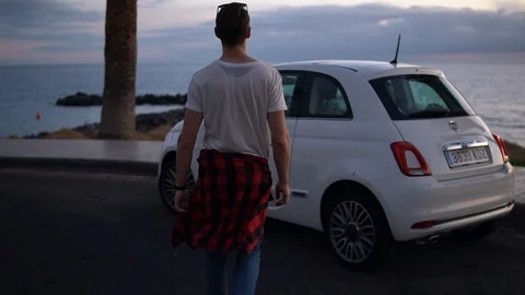 Man gets in white small car on the beach in the evening Stock Footage 105153337